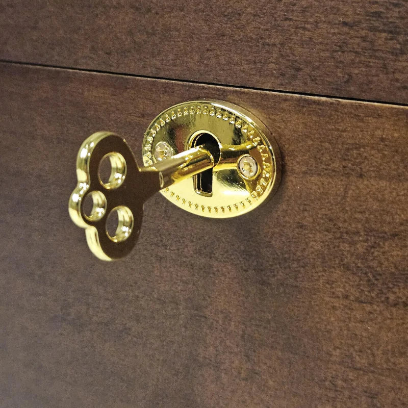 A close-up of a polished brass or gold-toned decorative lock set on a dark brown wooden surface, with a matching decorative key inserted.
