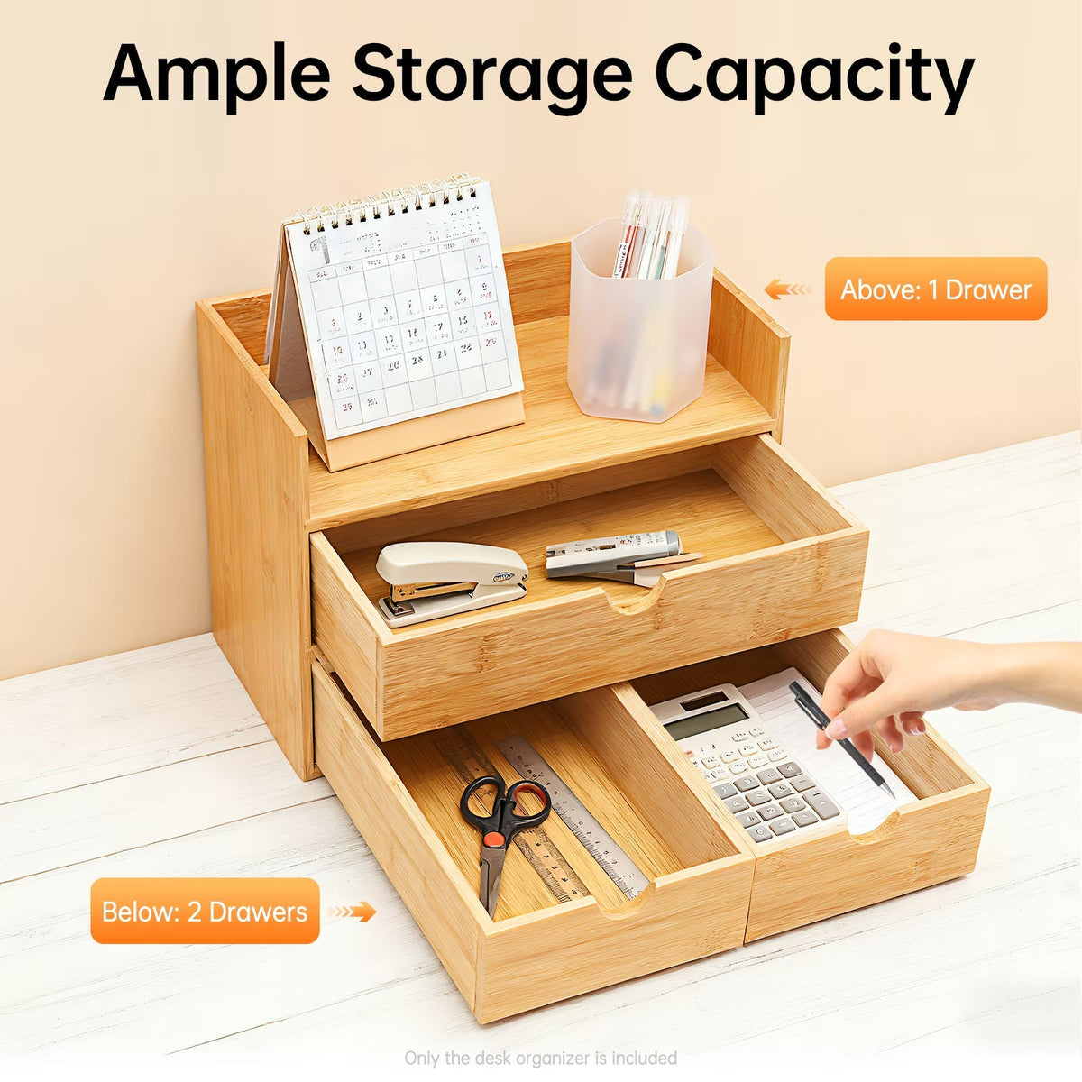 A light natural wood desktop organizer with two pull-out drawers and a top tray, shown on a white desk against a beige wall. The organizer contains office supplies including a calendar, pencil cup, stapler, scissors, ruler, calculator, and pen.