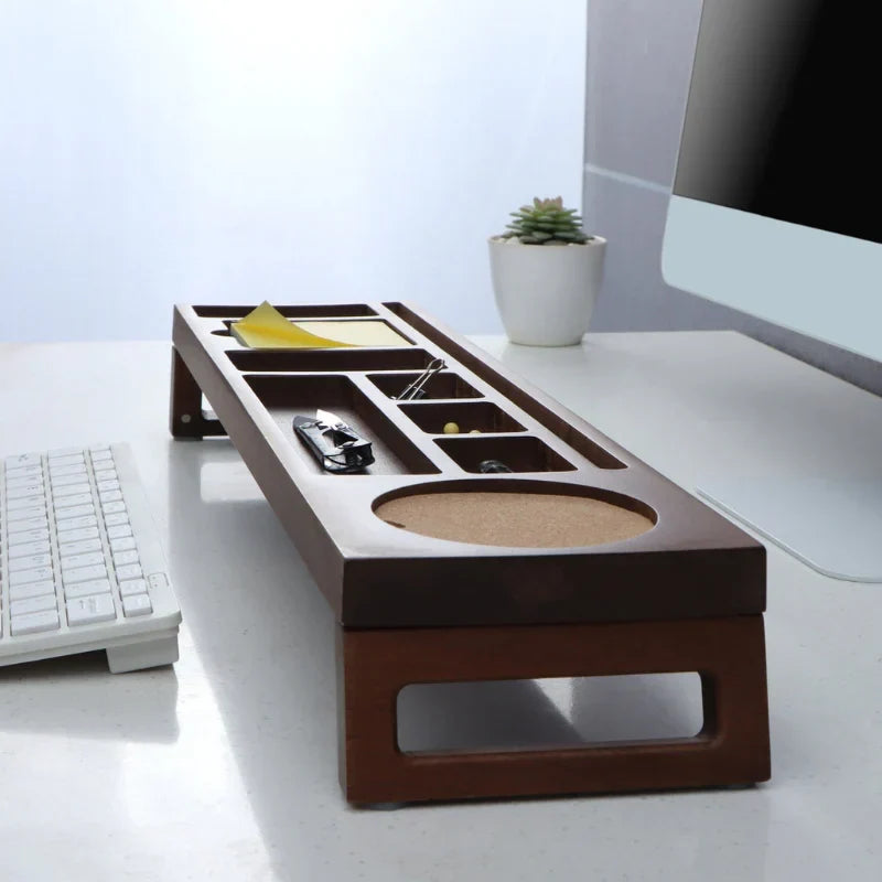 A dark brown wooden desk organizer with multiple compartments, a circular cork tray, and a raised keyboard stand, shown on a white desk next to a keyboard and computer monitor.