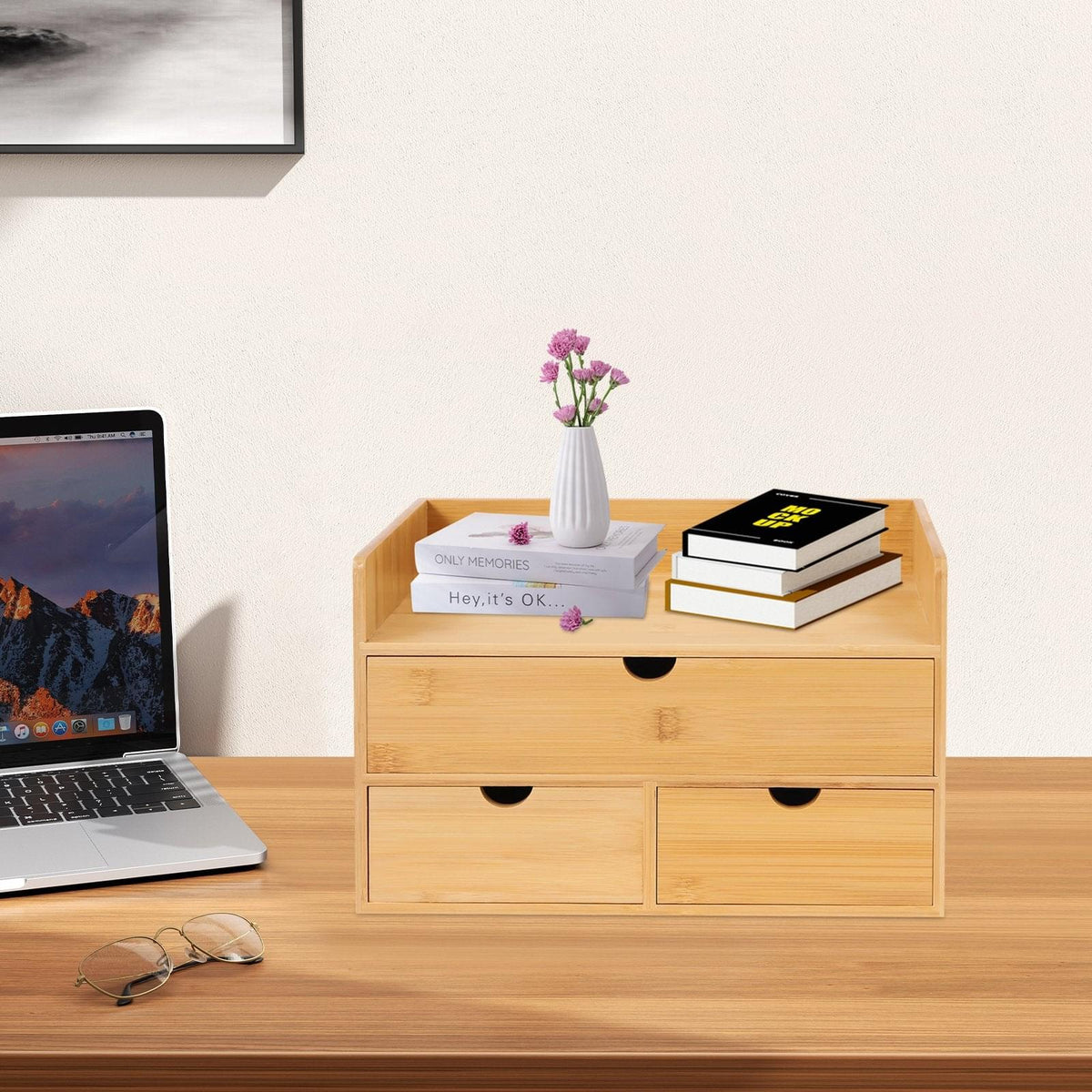 A light natural wood desktop organizer with two top drawers and two lower drawers, styled on a wooden desk with books, a small vase of flowers, and a laptop nearby.