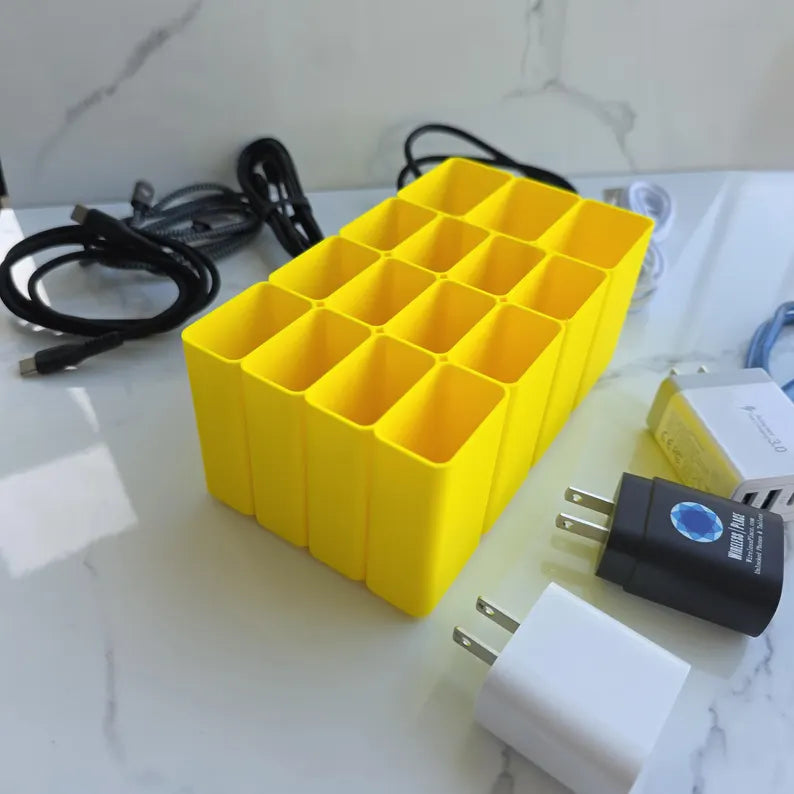 Yellow battery holder with multiple compartments on a marble surface with cables and a plug.